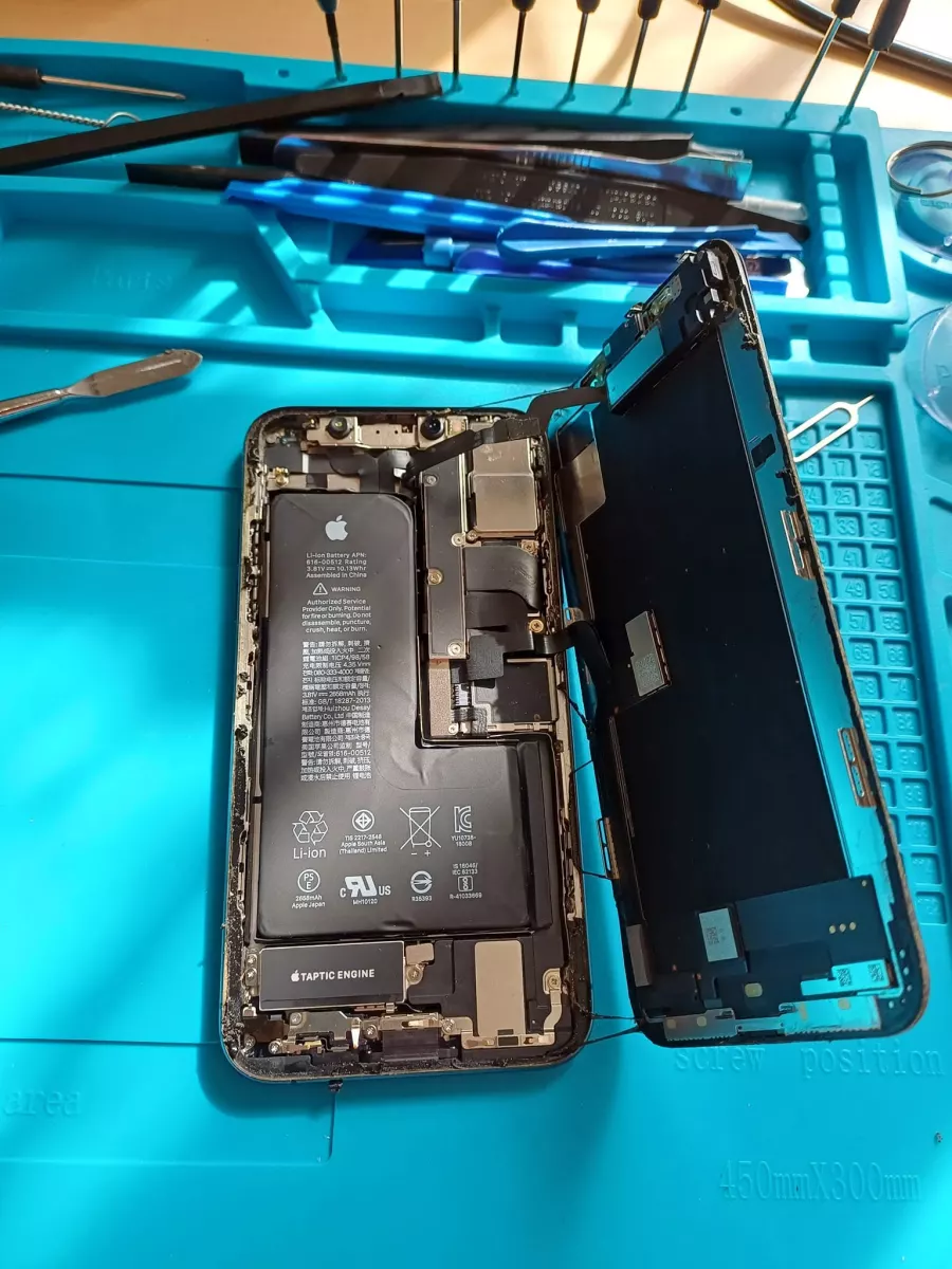 iPhone démonté, batterie et écran visibles, sur le tapis de l'atelier